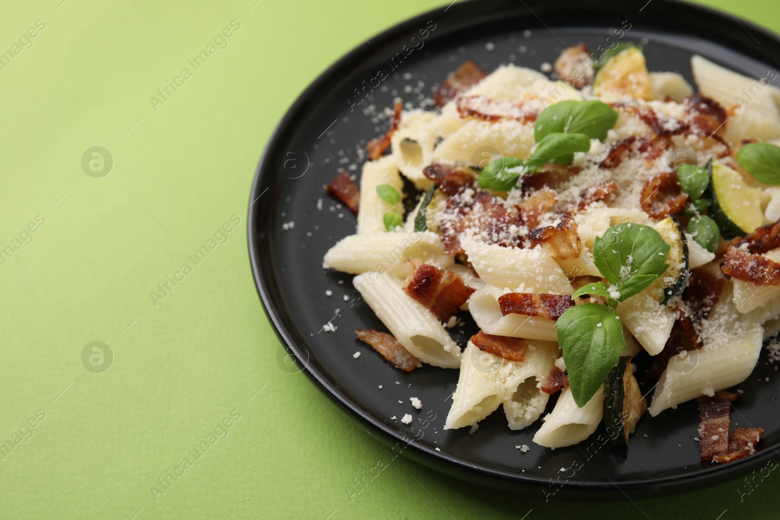 Photo of Tasty pasta with bacon and basil on light green table, closeup. Space for text