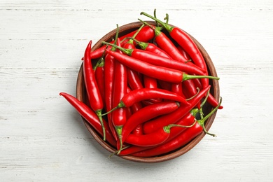 Photo of Wooden bowl with red hot chili peppers on white table, top view