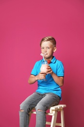 Photo of Little boy with glass of milk shake on stool against color background