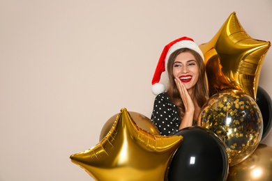 Photo of Happy woman in Santa hat with air balloons on beige background, space for text. Christmas party