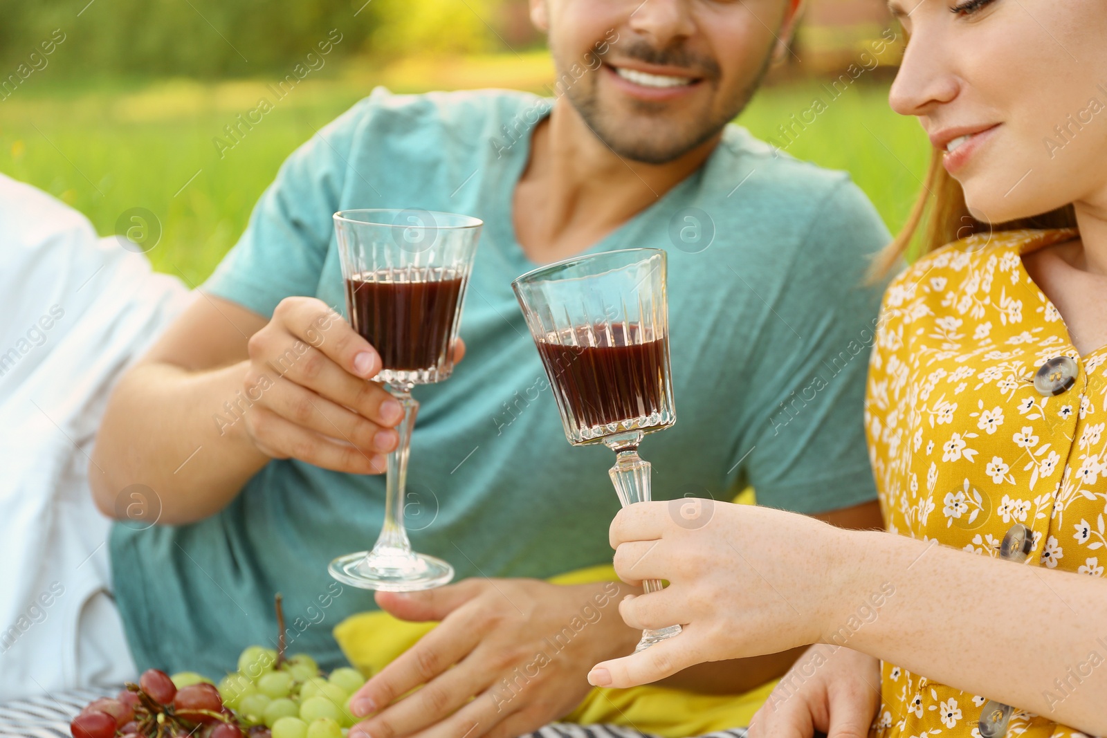 Photo of Young couple with glasses of wine having picnic outdoors, closeup