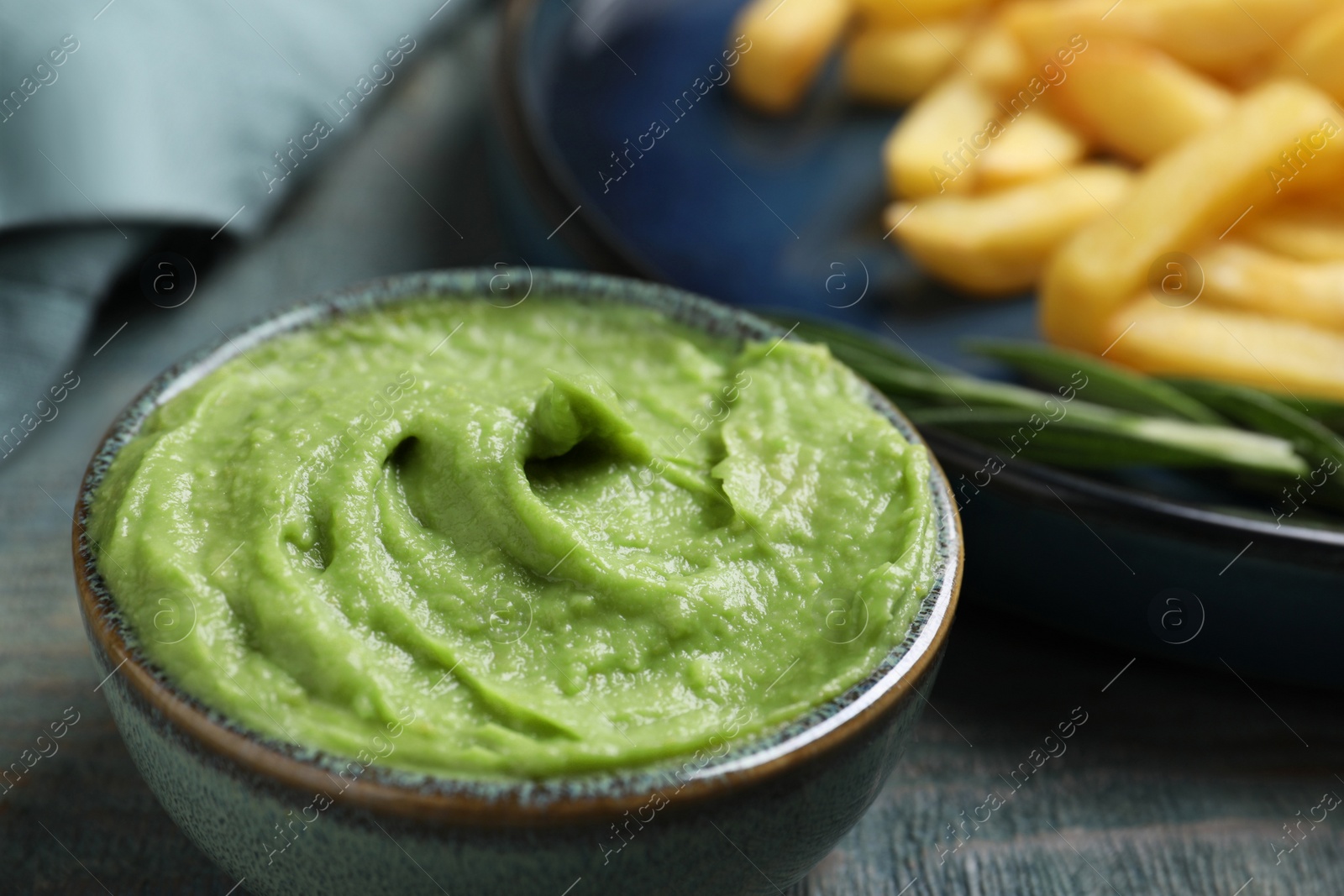 Photo of Plate with delicious french fries, avocado dip and rosemary served on grey wooden table, closeup