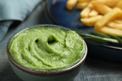 Photo of Plate with delicious french fries, avocado dip and rosemary served on grey wooden table, closeup