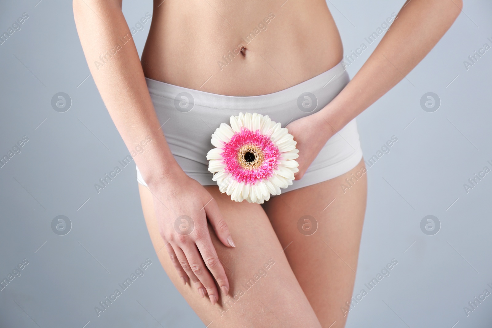 Photo of Young woman holding flower near underwear on grey background. Gynecology