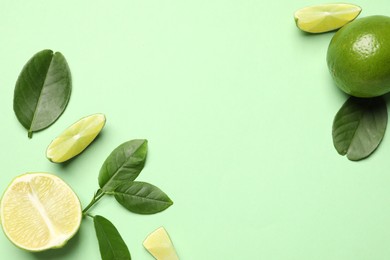 Photo of Whole and cut fresh ripe limes with leaves on light green background, flat lay