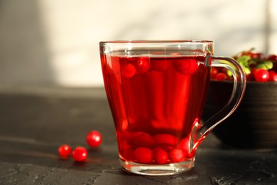 Photo of Tasty hot cranberry tea in glass cup and fresh berries on black textured table