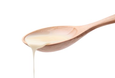 Photo of Pouring condensed milk from wooden spoon isolated on white