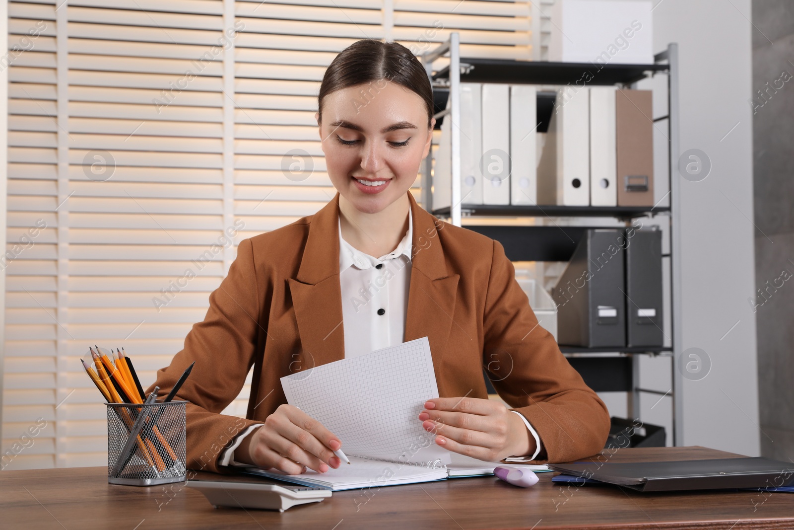 Photo of Happy woman taking notes at wooden table in office