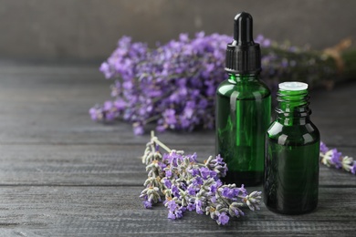 Photo of Bottles with natural lavender oil and flowers on wooden table against grey background, closeup view. Space for text