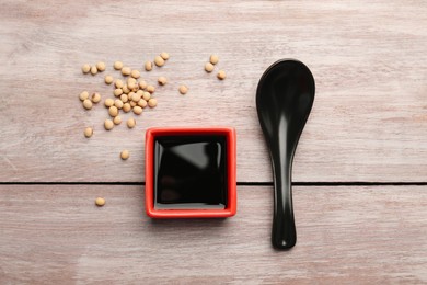 Photo of Soy sauce in bowl, soybeans and spoon on wooden table, flat lay