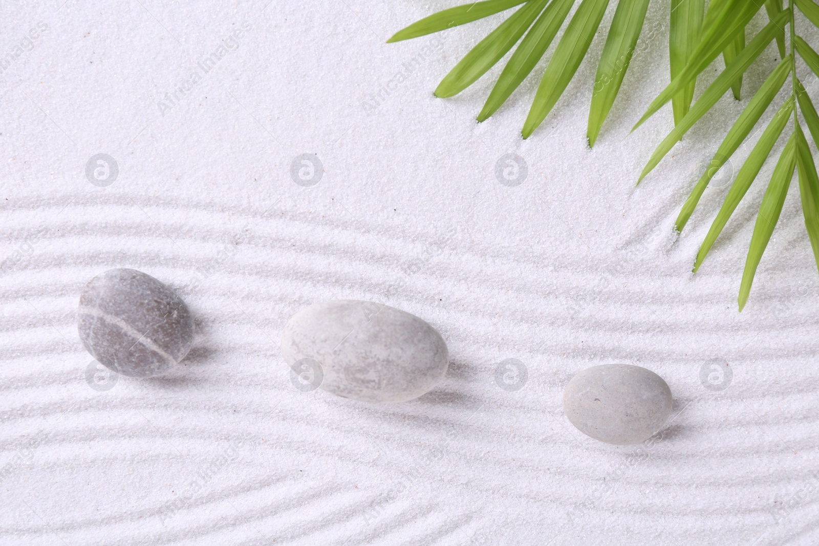 Photo of Zen garden stones and green leaves on white sand with pattern, flat lay