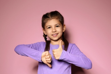 Photo of Little girl showing THUMB UP and DOWN gesture in sign language on color background