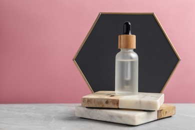 Photo of Bottle of face serum with marble boards on grey table against pink background. Space for text