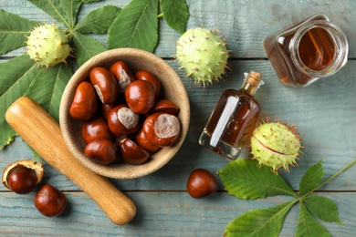 Photo of Mortar with pestle, chestnuts and essential oil on blue wooden table, flat lay