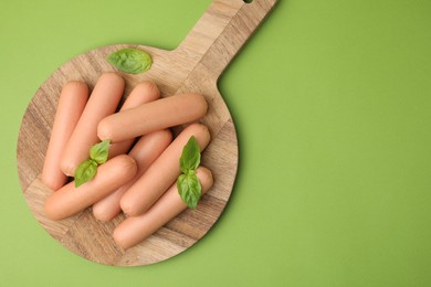 Photo of Delicious boiled sausages and basil on green table, top view. Space for text