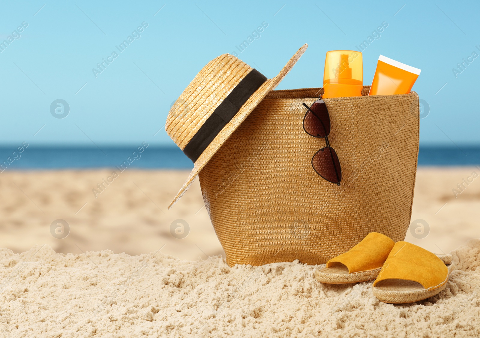 Image of Stylish bag with different accessories on sandy beach near ocean