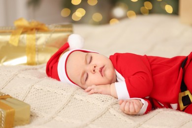 Photo of Cute baby in Christmas costume sleeping on knitted blanket against blurred festive lights. Winter holiday