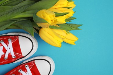 Pair of new stylish red sneakers and beautiful tulips on light blue background, flat lay. Space for text