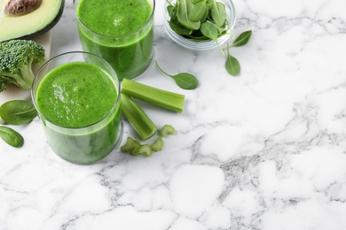 Photo of Delicious green juice and fresh ingredients on white marble table, above view. Space for text