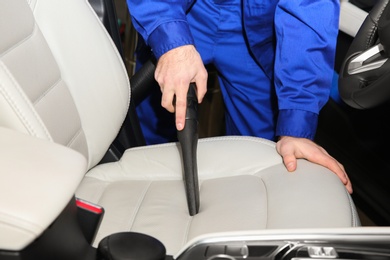 Closeup of worker vacuuming automobile seat, view from inside. Car wash service