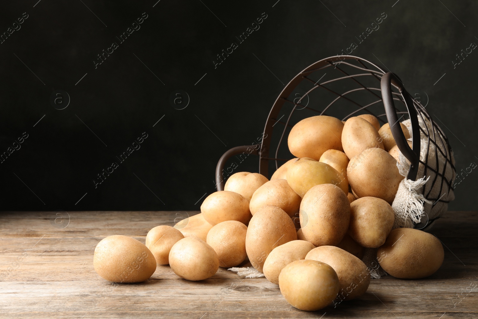 Photo of Raw fresh organic potatoes on wooden table against dark background. Space for text