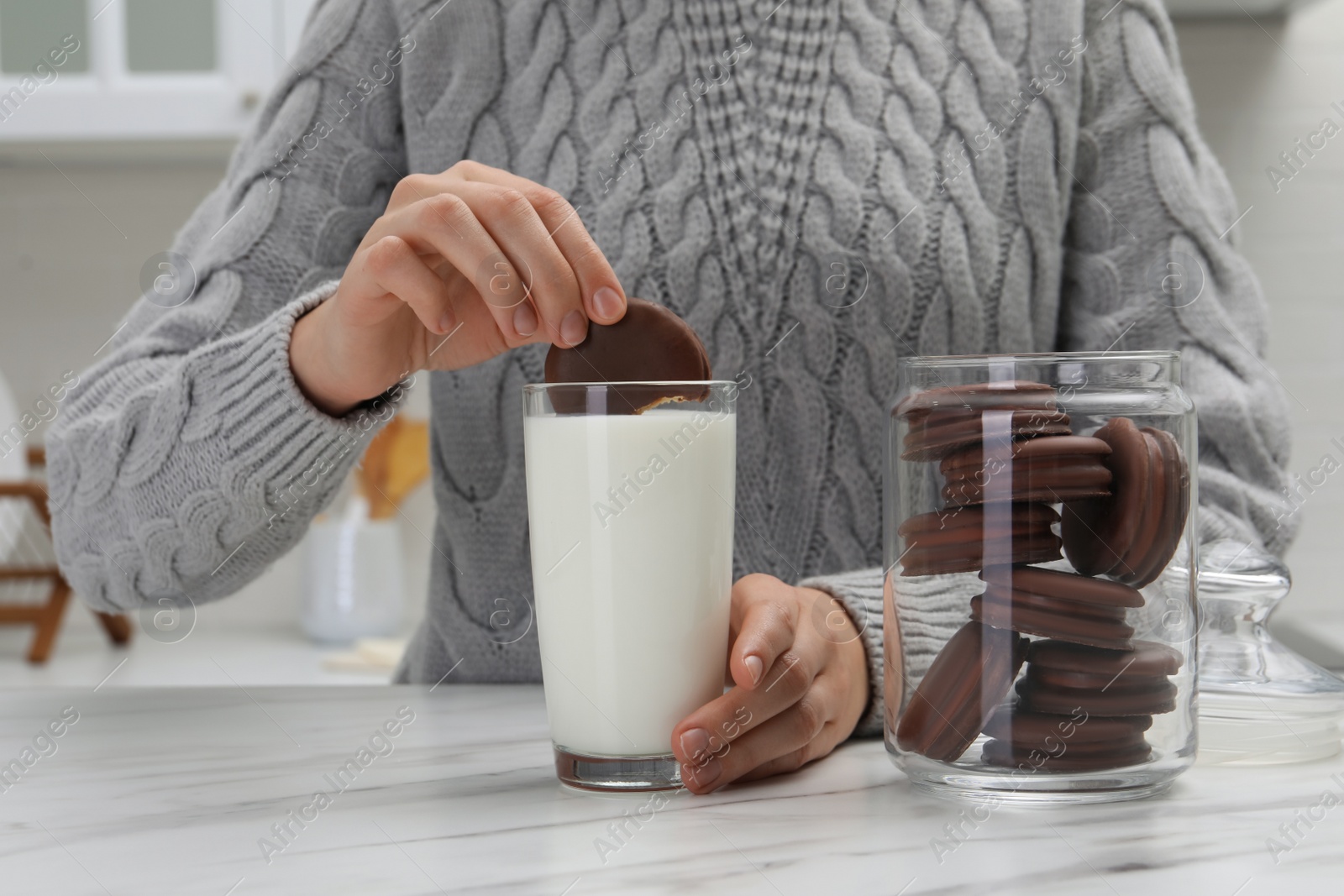 Photo of Woman dipping delicious choco pie into glass of milk at white marble table, closeup