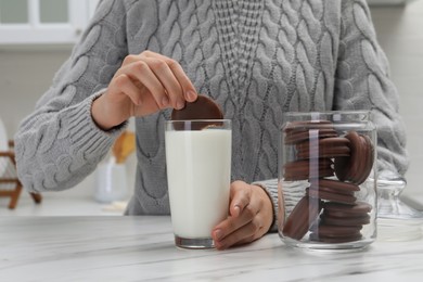 Photo of Woman dipping delicious choco pie into glass of milk at white marble table, closeup