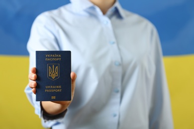 Photo of Woman holding Ukrainian travel passport against national flag, closeup. International relationships