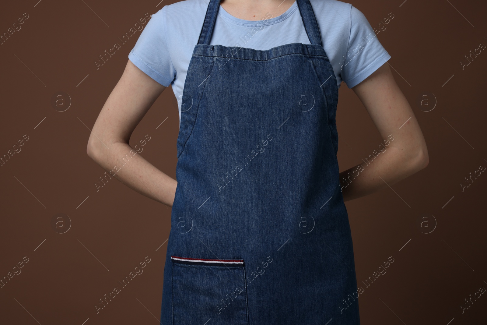 Photo of Woman wearing kitchen apron on brown background, closeup. Mockup for design