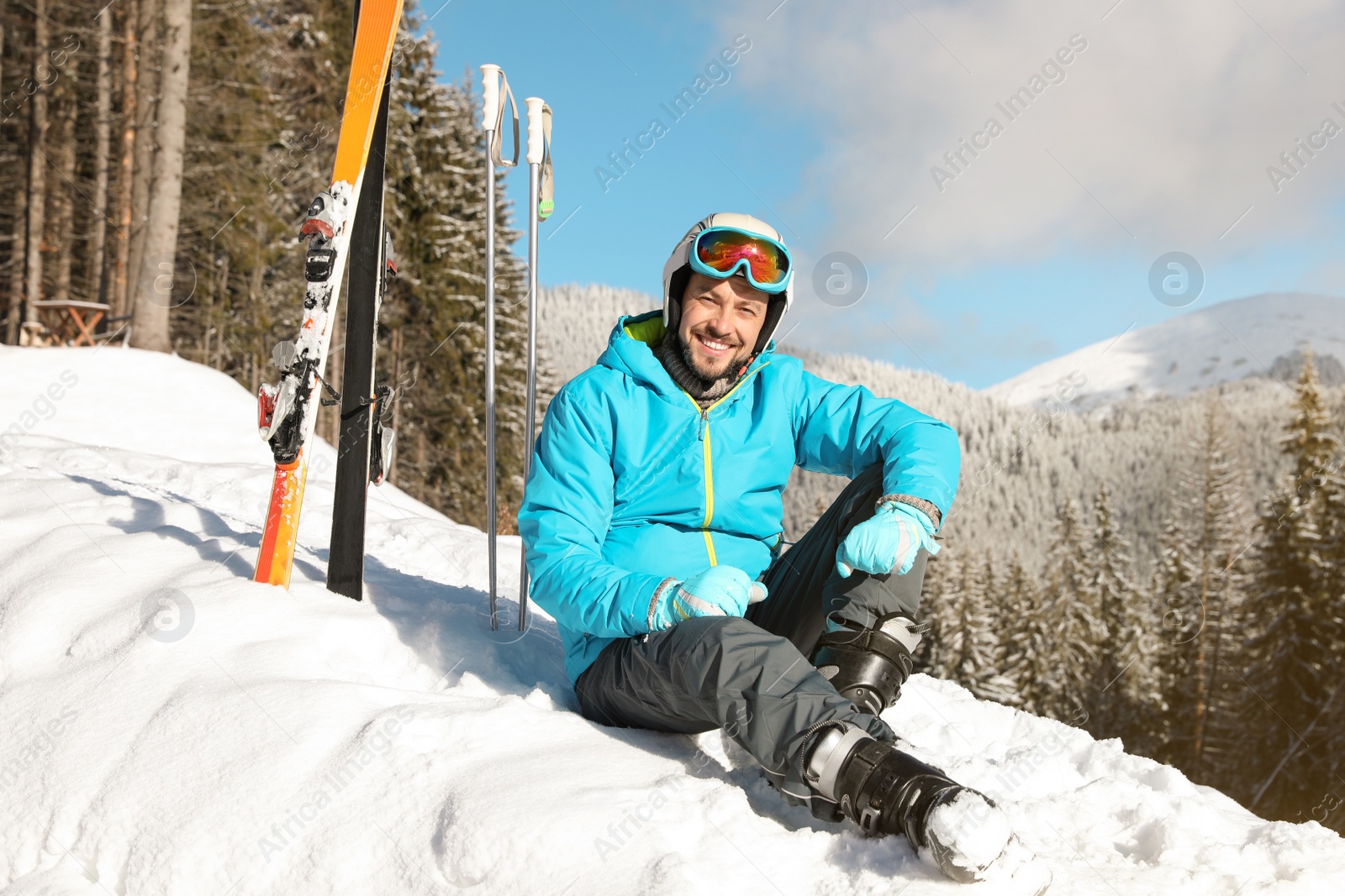 Photo of Man with ski equipment sitting on snow in mountains. Winter vacation