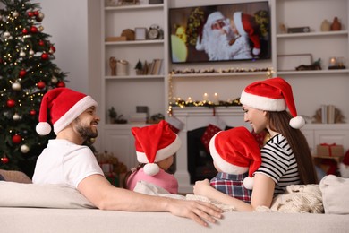 Photo of Happy family wearing Christmas hats spending time near TV in cosy room. Winter holidays atmosphere