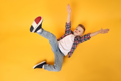 Photo of Happy little boy dancing on yellow background, top view