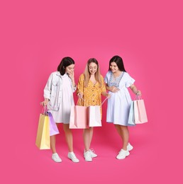 Happy pregnant women with shopping bags on pink background