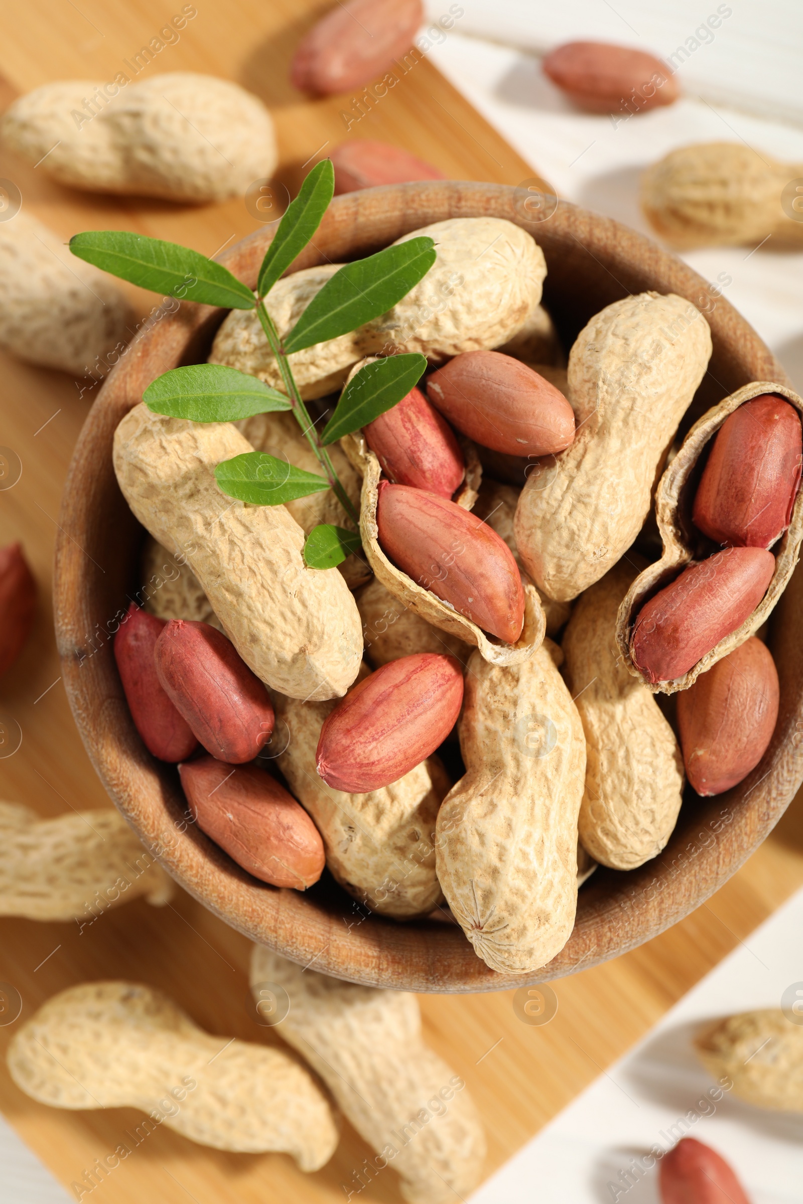 Photo of Fresh unpeeled peanuts in bowl and twig on table, top view