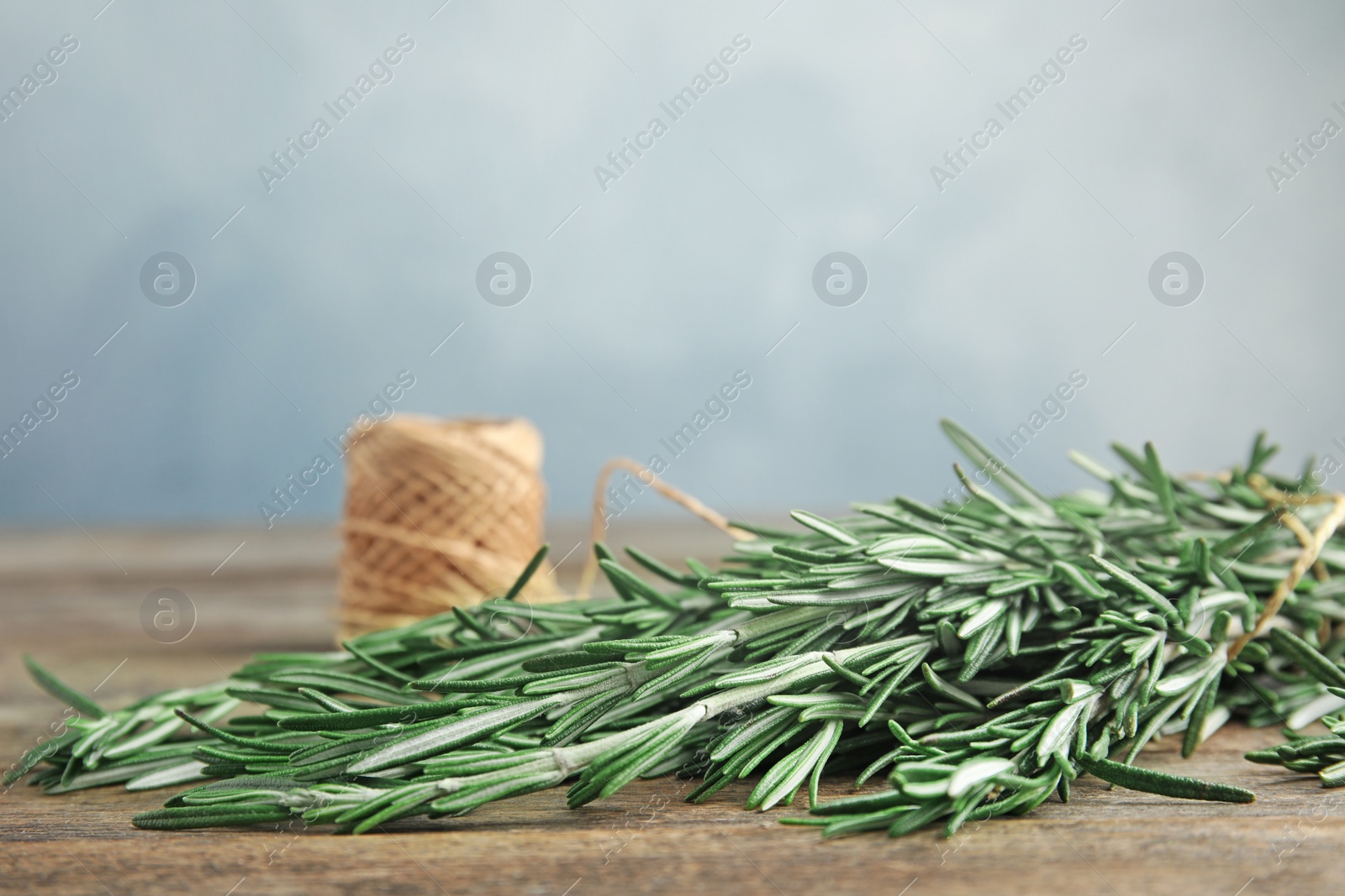 Photo of Fresh rosemary branches and twine on wooden table. Space for text