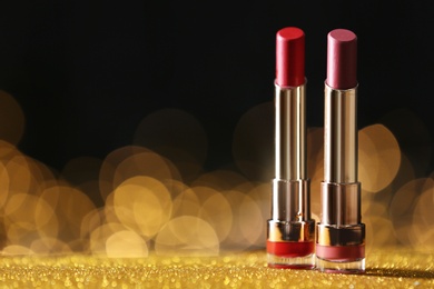 Photo of Bright lipsticks on table with gold glitter against blurred lights, space for text