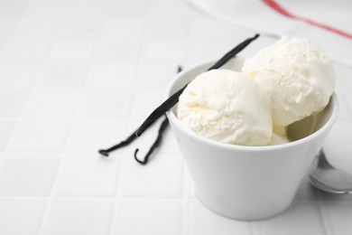 Delicious ice cream and vanilla pods on white tiled table, closeup. Space for text