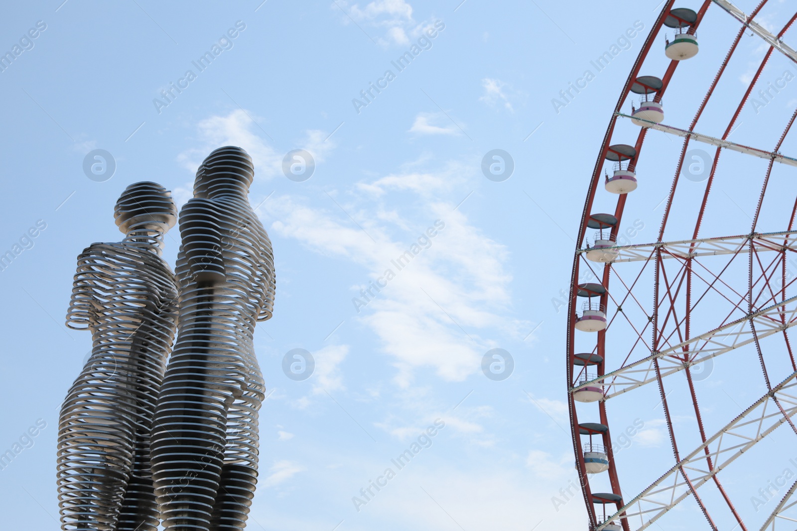 Photo of BATUMI, GEORGIA - JUNE 14, 2022: Movable sculptural composition Ali and Nino near Ferris wheel, low angle view