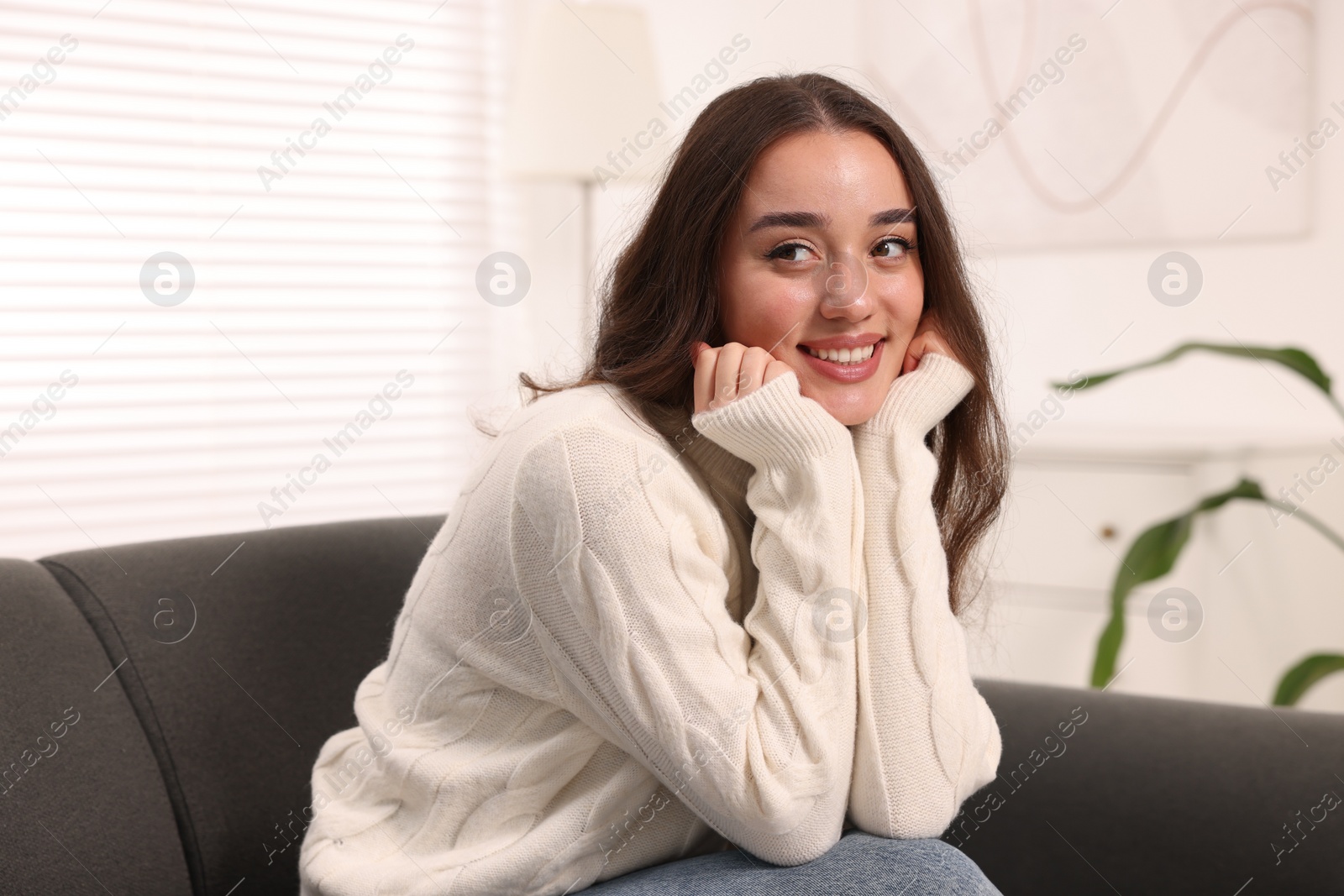 Photo of Beautiful young woman in stylish warm sweater on sofa at home