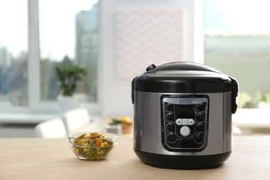 Modern multi cooker and ingredients on table in kitchen. Space for text