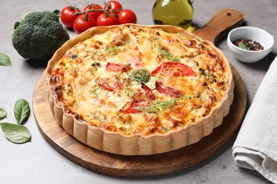 Tasty cheese quiche and ingredients on light grey table