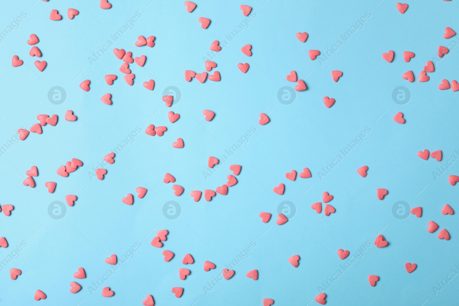 Photo of Bright heart shaped sprinkles on light blue background, flat lay