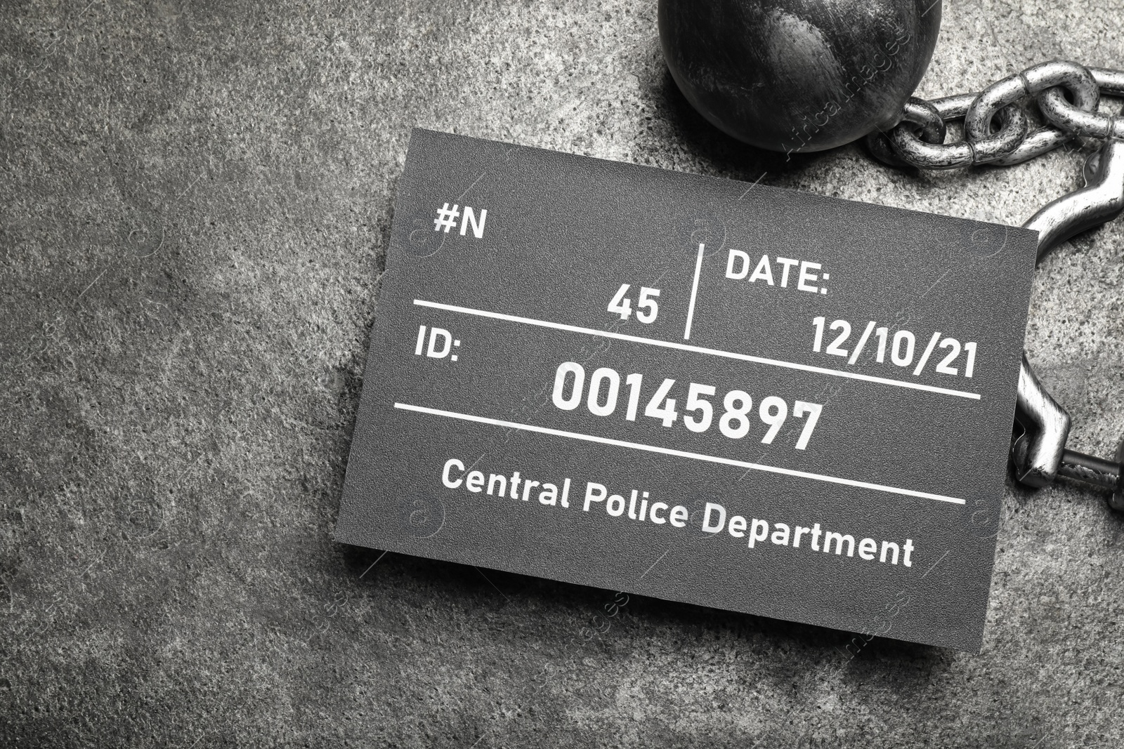 Photo of Metal ball with chain and mugshot letter board on grey table, flat lay