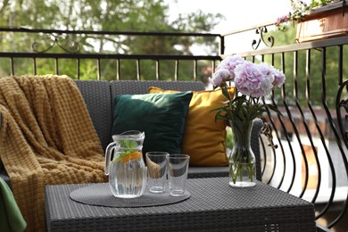 Photo of Rattan table with jug of water, glasses and beautiful flowers on terrace