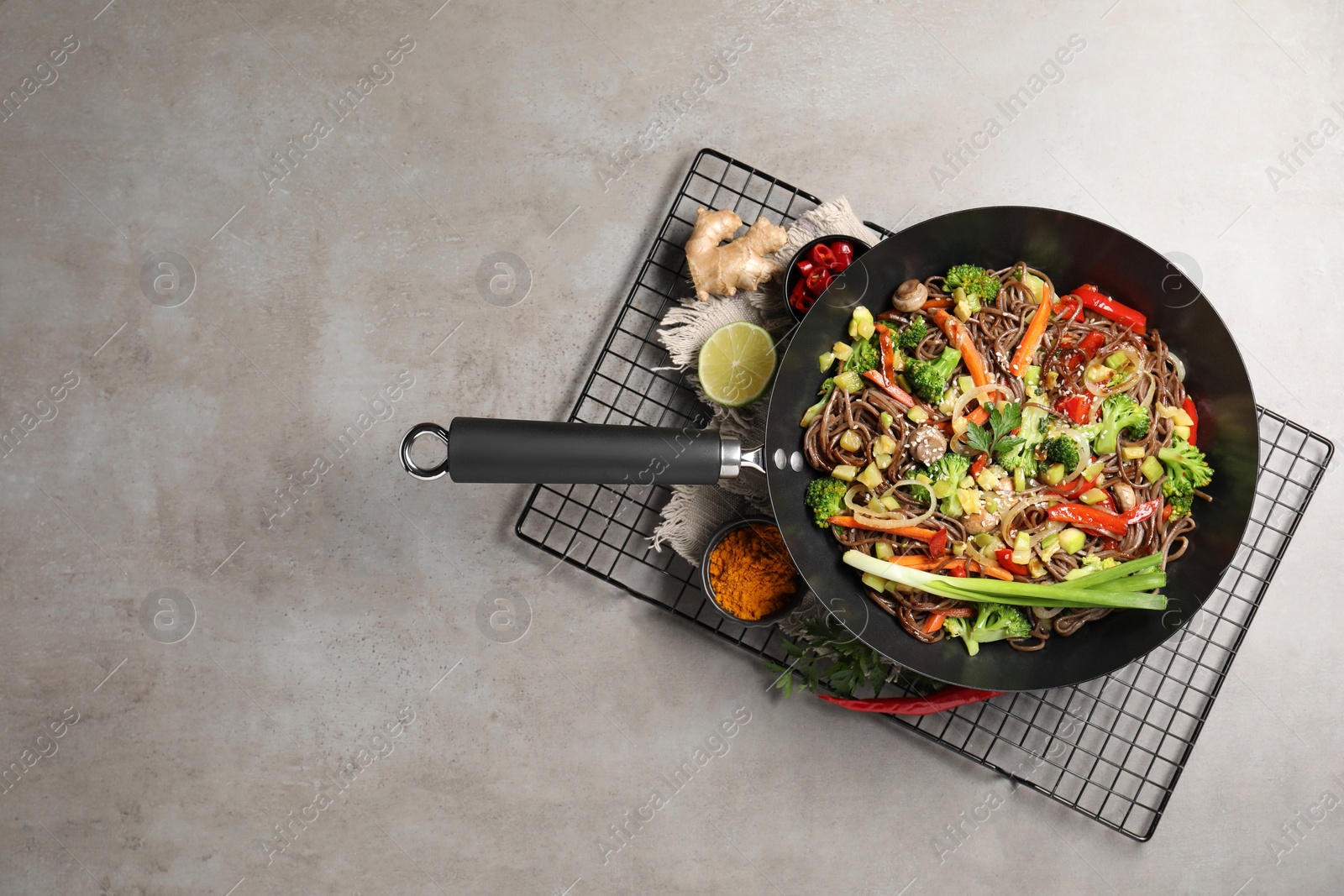 Photo of Stir-fry. Tasty noodles with meat in wok and ingredients on grey textured table, flat lay. Space for text