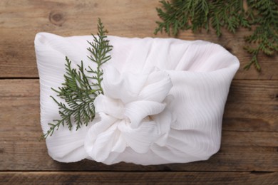 Photo of Furoshiki technique. Gift packed in white fabric and thuja branches on wooden table, top view