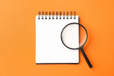 Photo of Magnifier glass and empty notebook on orange background, flat lay with space for text. Find keywords concept