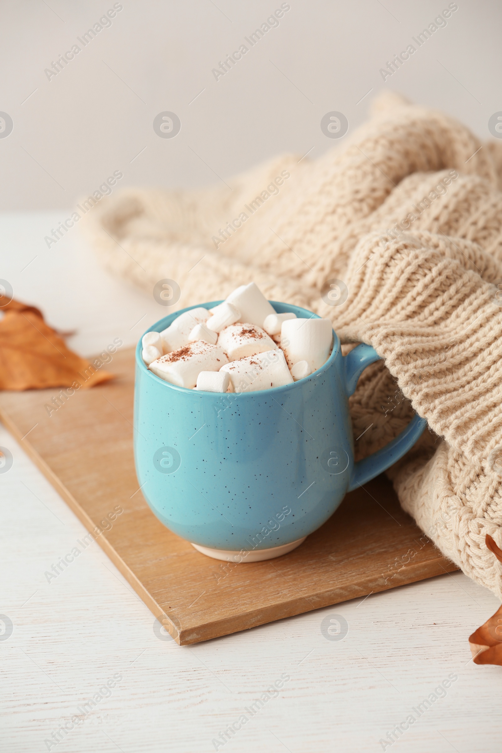 Photo of Cup of hot cozy drink with marshmallows and autumn sweater on table