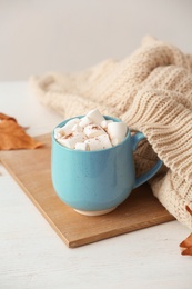 Photo of Cup of hot cozy drink with marshmallows and autumn sweater on table
