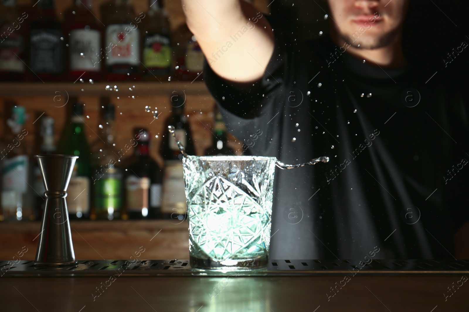 Photo of Bartender preparing fresh alcoholic cocktail at bar counter, focus on glass